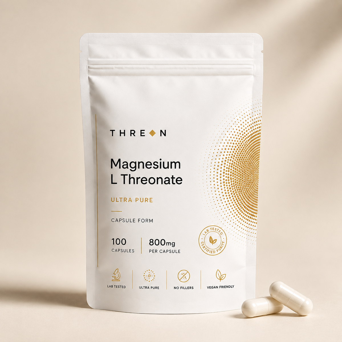 A white stand-up pouch of Threon Magnesium L Threonate capsules on a warm beige background, with two capsules placed in front. The package features gold text and a gold circular dot pattern, and the Threon brand name is clearly visible.