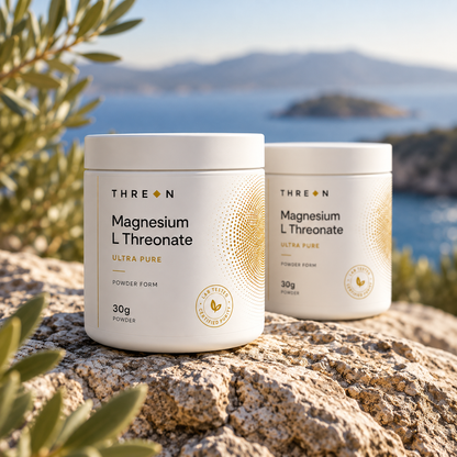 Two white jars of THREON Magnesium L Threonate powder placed on a rock with a blurred coastal landscape in the background.